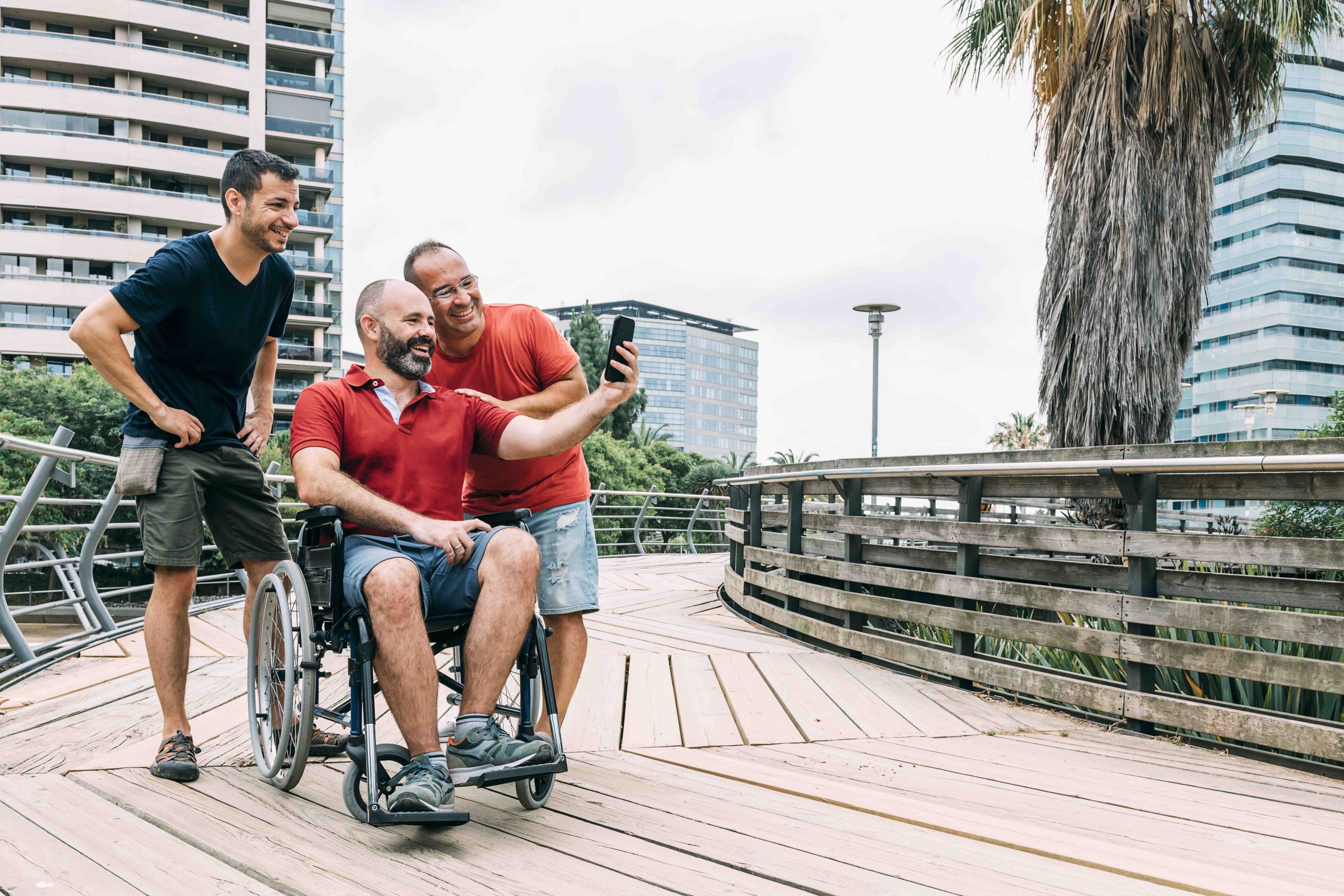 disabled man in wheelchair taking a selfie with his phone with two friends during a walk, concept of friendship and integration of people with disabilities and reduced mobility problems